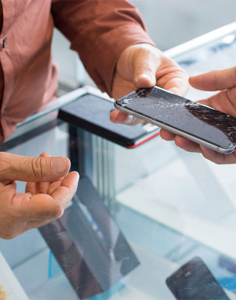 Two individuals are examining a damaged smartphone. The screen appears to be cracked and wet.