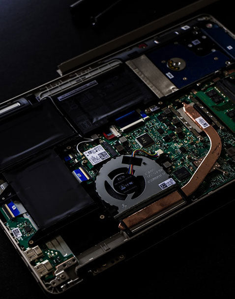 The image displays the internal components of a laptop or computer. Visible elements include the motherboard with its green circuits, a cooling fan, the battery, and various connectors and chips. The device appears to be opened for repair or inspection.